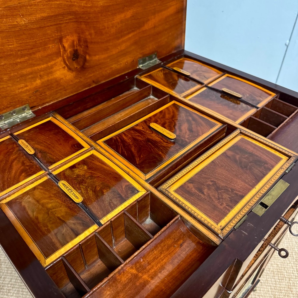A late Georgian mahogany work table with an open hinged lid revealing fitted interior compartments, pleated fabric side panels, and square tapered legs on brass castors. View II