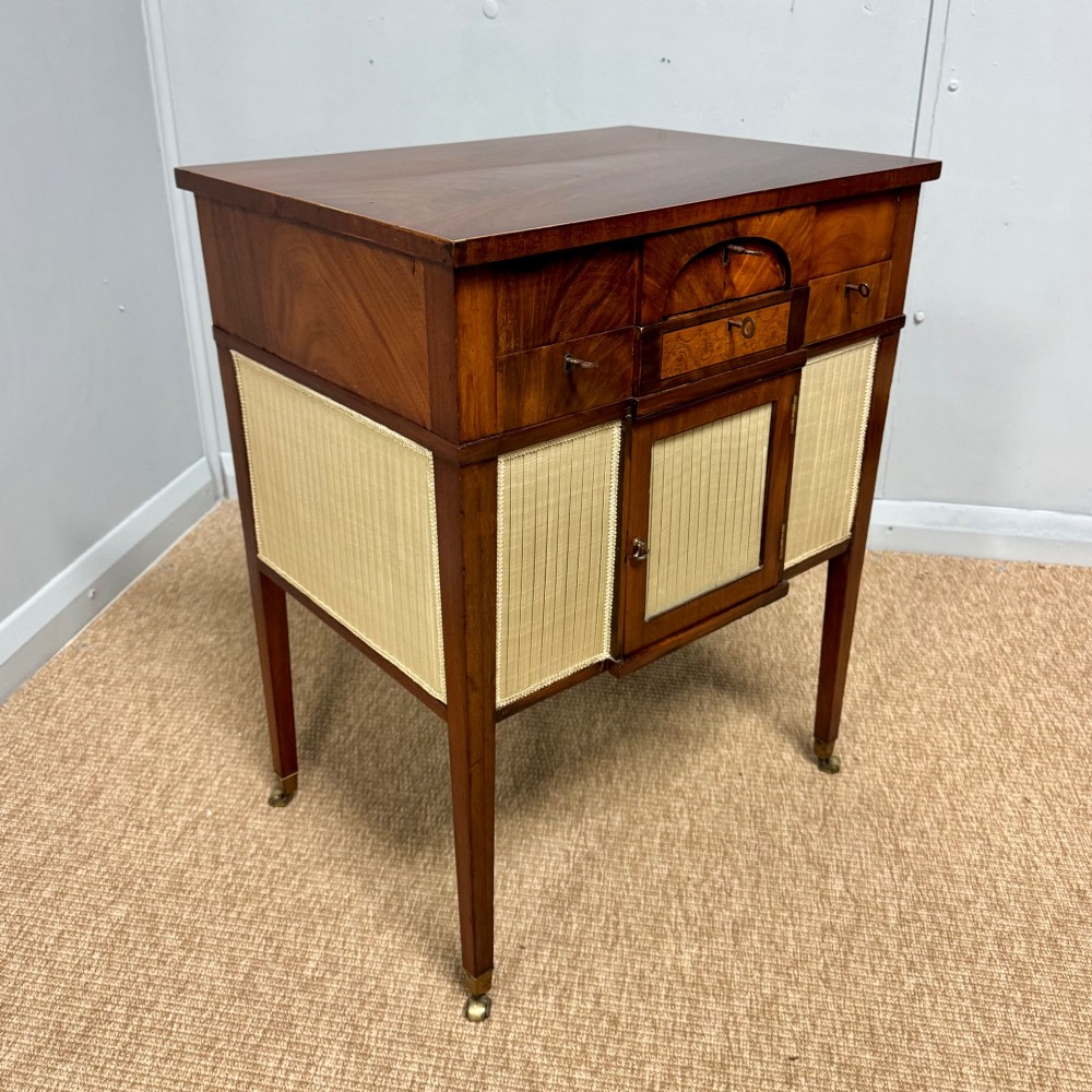 A late Georgian mahogany work table with an open hinged lid revealing fitted interior compartments, pleated fabric side panels, and square tapered legs on brass castors. View V
