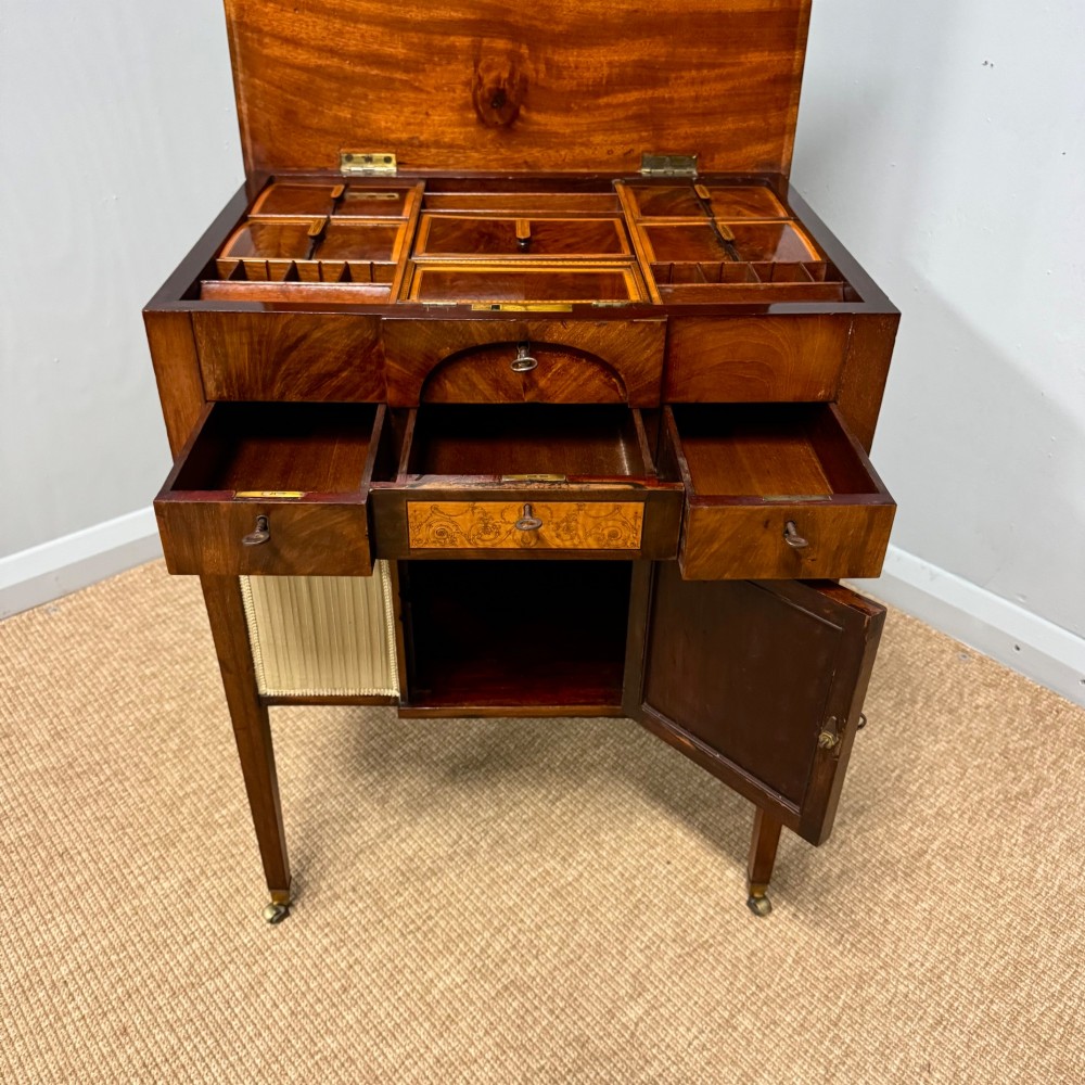 A late Georgian mahogany work table with an open hinged lid revealing fitted interior compartments, pleated fabric side panels, and square tapered legs on brass castors. View VI