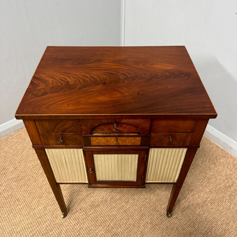 A late Georgian mahogany work table with an open hinged lid revealing fitted interior compartments, pleated fabric side panels, and square tapered legs on brass castors. View VII