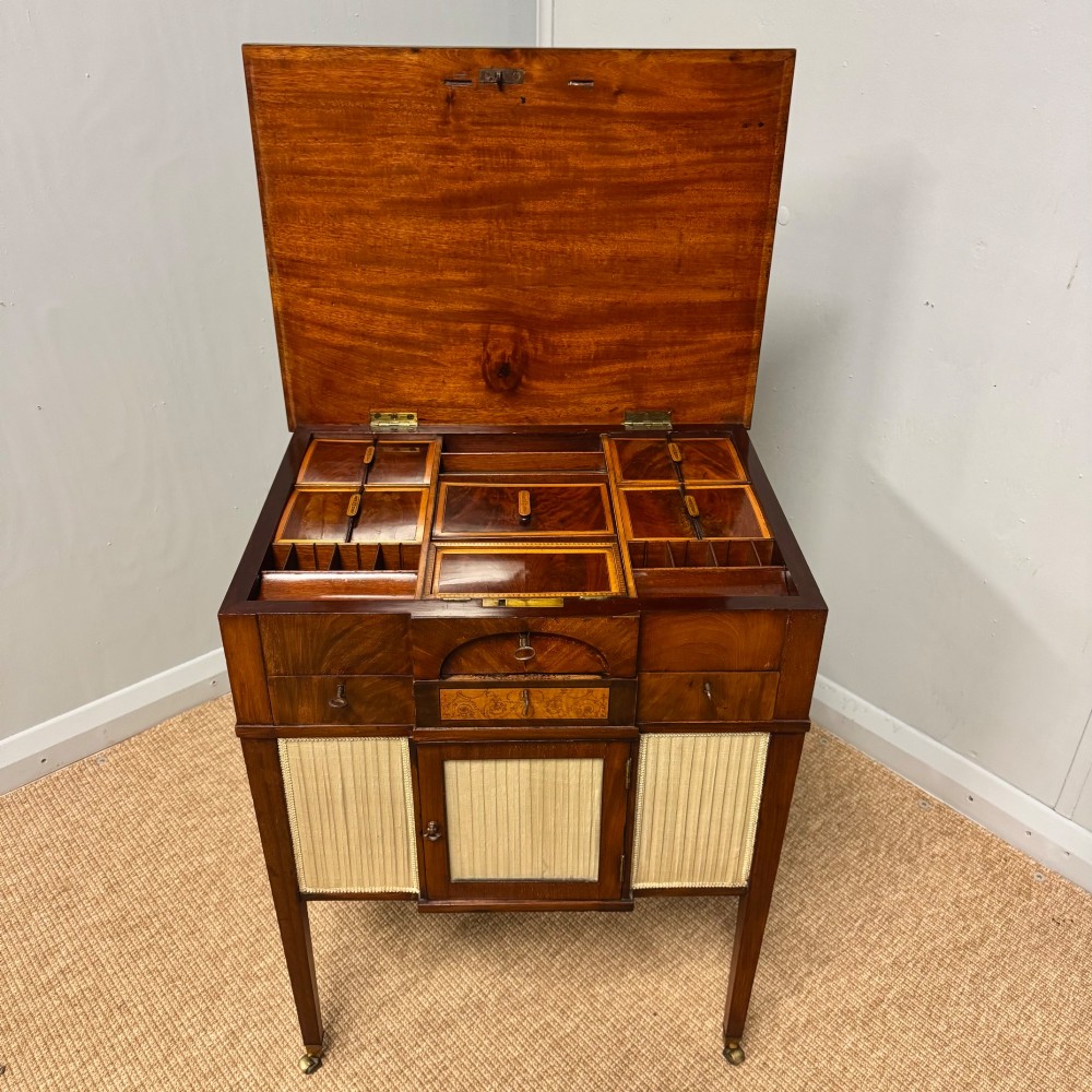 A late Georgian mahogany work table with an open hinged lid revealing fitted interior compartments, pleated fabric side panels, and square tapered legs on brass castors. View X