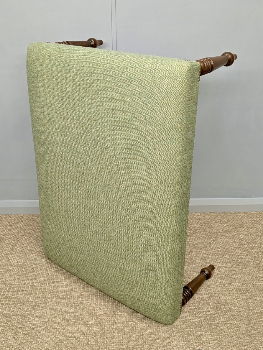 A square low footstool upholstered in sage green herringbone wool tweed with four turned dark wood legs and brass stud detailing. View IV