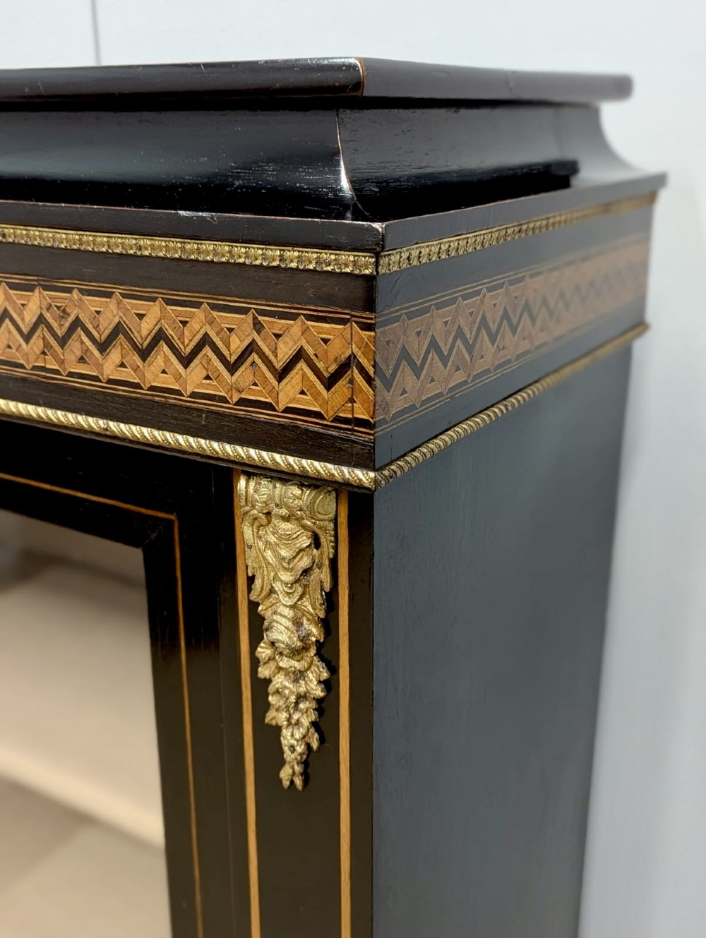 A black ebonised two-door glazed cabinet featuring a moulded caddy top, brass ormolu corner mounts, and a band of geometric marquetry inlay. View III