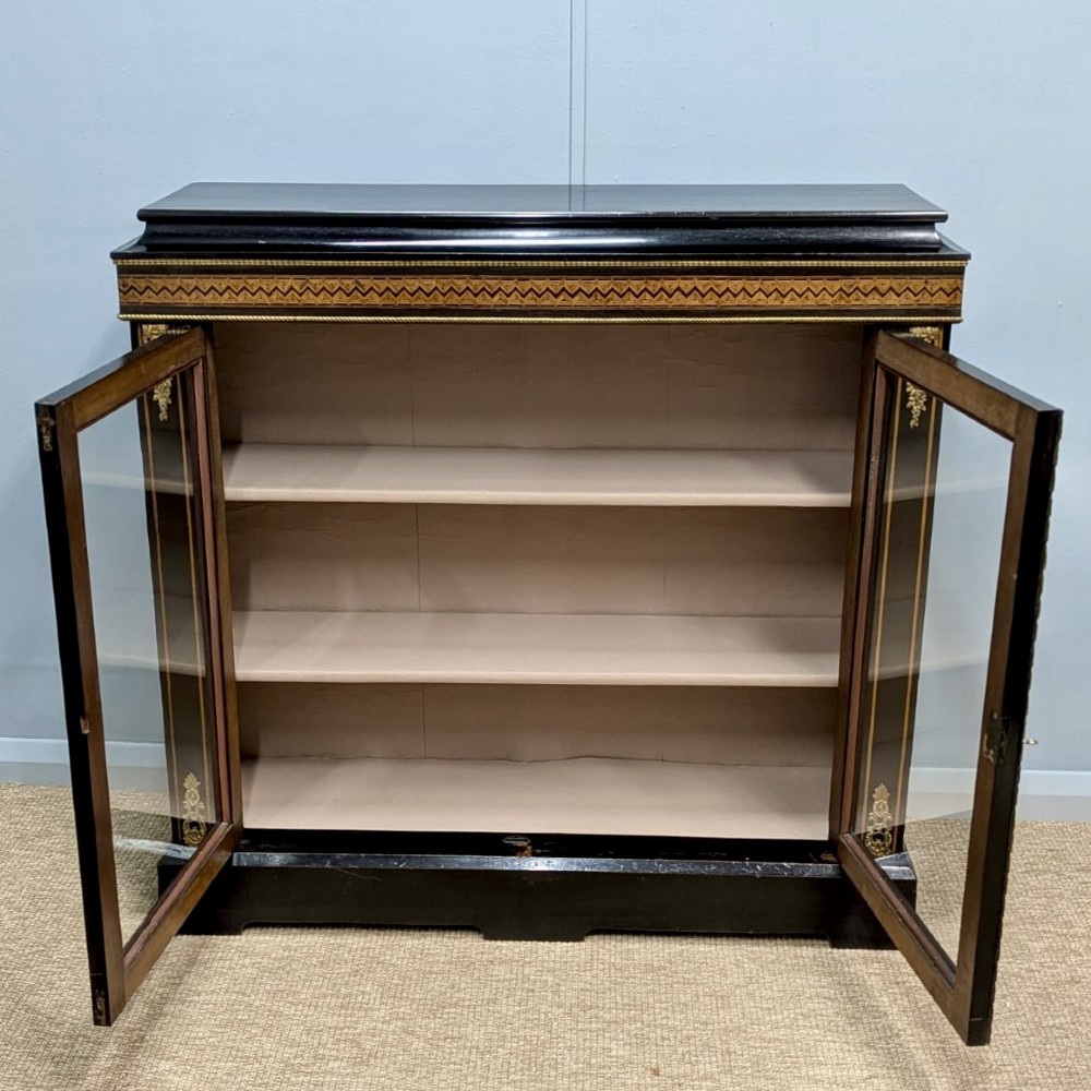 A black ebonised two-door glazed cabinet featuring a moulded caddy top, brass ormolu corner mounts, and a band of geometric marquetry inlay. View IV