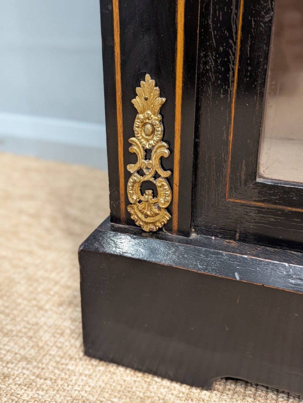 A black ebonised two-door glazed cabinet featuring a moulded caddy top, brass ormolu corner mounts, and a band of geometric marquetry inlay. View VII