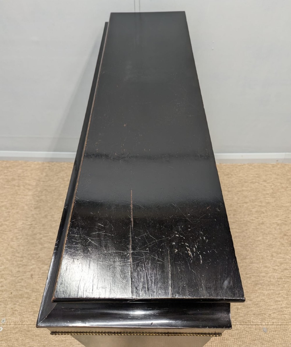 A black ebonised two-door glazed cabinet featuring a moulded caddy top, brass ormolu corner mounts, and a band of geometric marquetry inlay. View X
