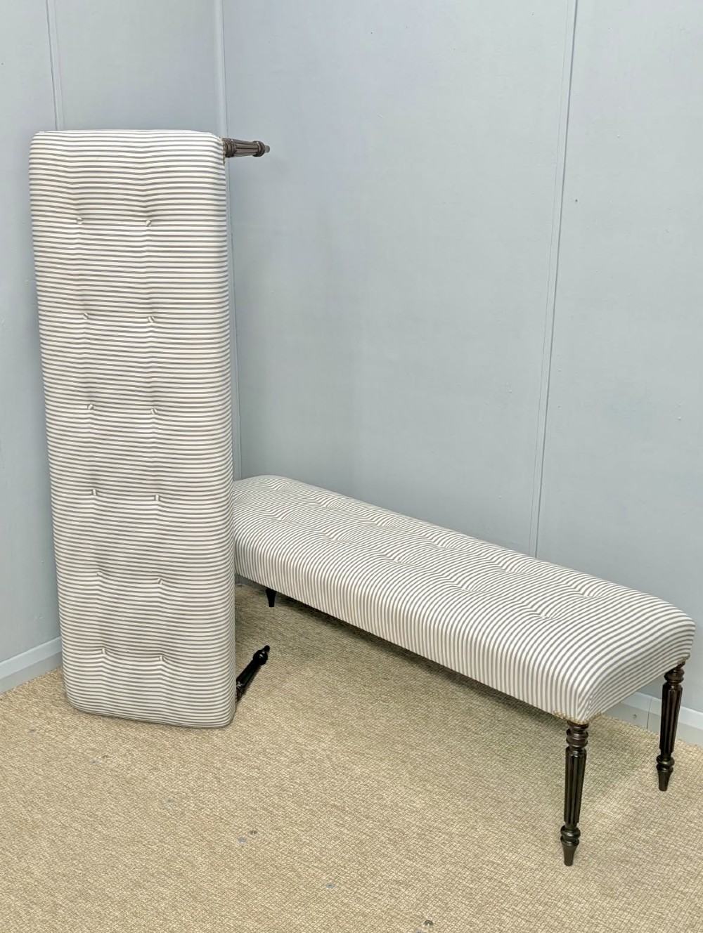 A pair of long upholstered benches featuring grey and white striped ticking fabric with deep button tufting set upon dark turned and fluted timber legs. View III