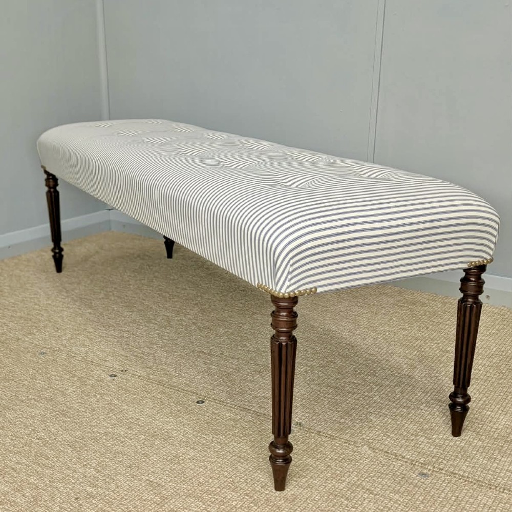 A pair of long upholstered benches featuring grey and white striped ticking fabric with deep button tufting set upon dark turned and fluted timber legs. View V