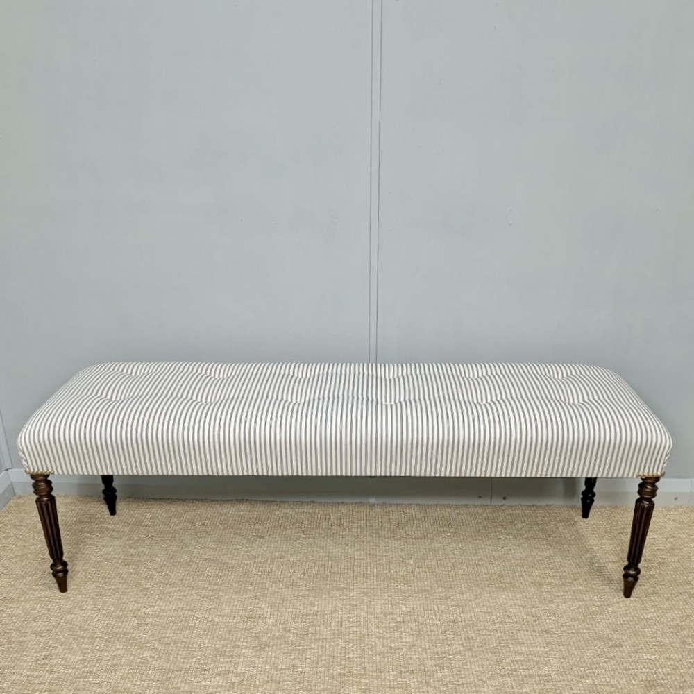 A pair of long upholstered benches featuring grey and white striped ticking fabric with deep button tufting set upon dark turned and fluted timber legs. View VI