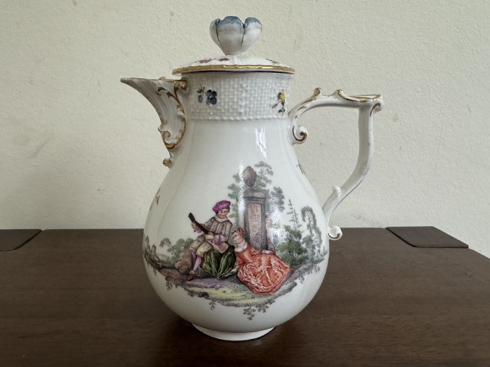 An 18th-century Meissen white hard-paste porcelain milk jug and cover featuring hand-painted figures in a landscape, floral sprigs, a flower finial, and a gilt scroll handle.
