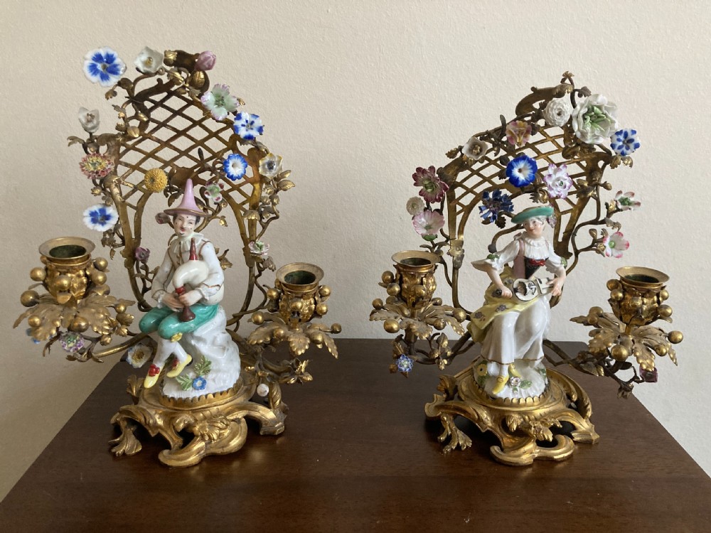 A pair of 18th-century Rococo gilt bronze candelabra featuring seated Meissen porcelain musician figures against floral trellis backdrops.