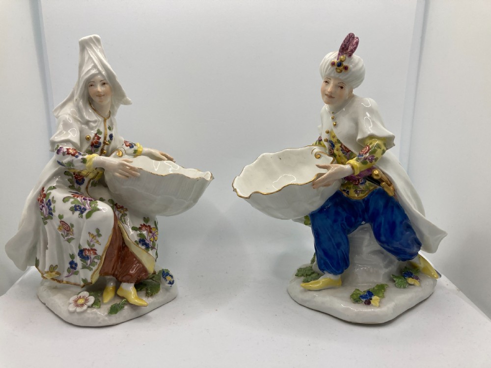 A pair of 18th-century Meissen hard-paste porcelain figures wearing Ottoman garments, each holding a scallop shell-shaped dish.