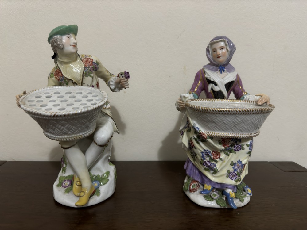 A pair of 18th-century Meissen hard-paste porcelain figures of a seated man and woman holding lattice-patterned basket flower holders with pierced tops.