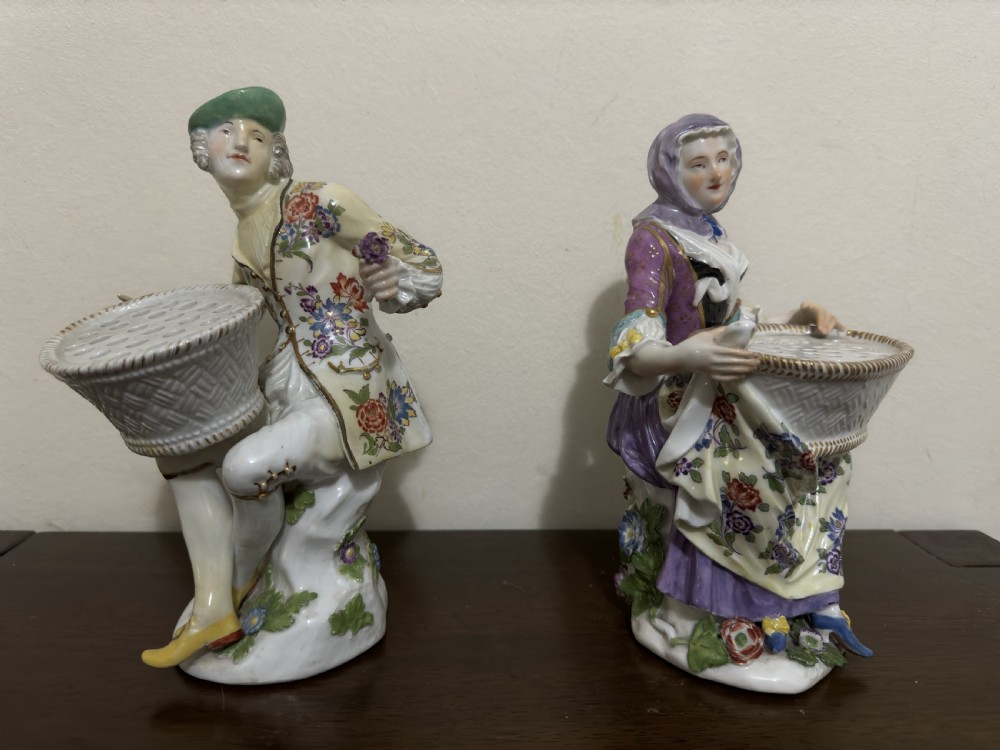 A pair of 18th-century Meissen hard-paste porcelain figures of a seated man and woman holding lattice-patterned basket flower holders with pierced tops. View II