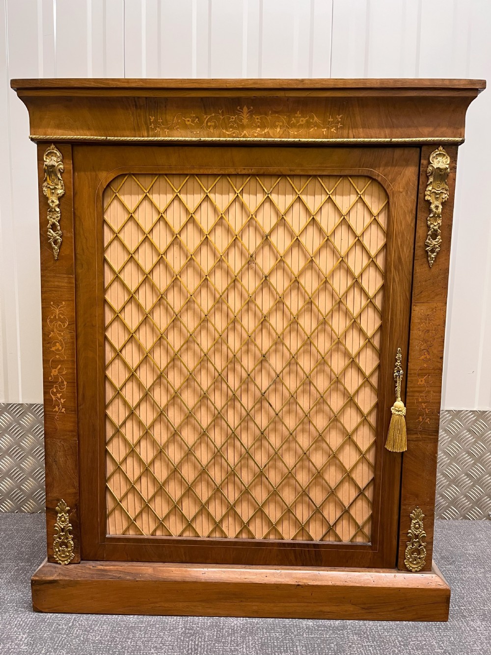 A Regency rosewood side cabinet featuring a brass lattice door with pleated fabric backing, ornate brass mounts, and brass marquetry inlays.
