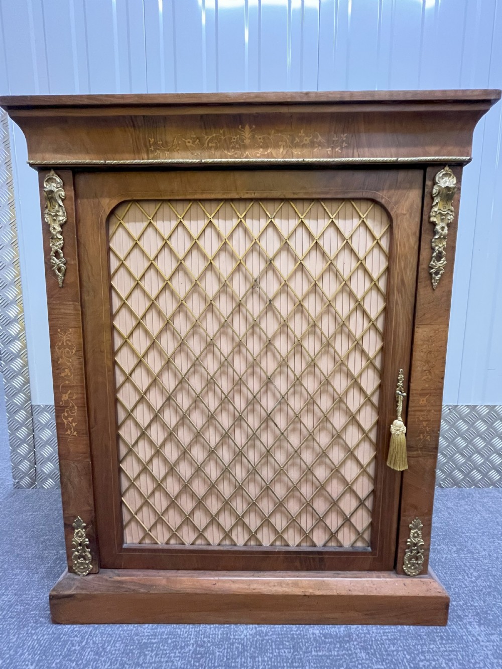 A Regency rosewood side cabinet featuring a brass lattice door with pleated fabric backing, ornate brass mounts, and brass marquetry inlays. View VI
