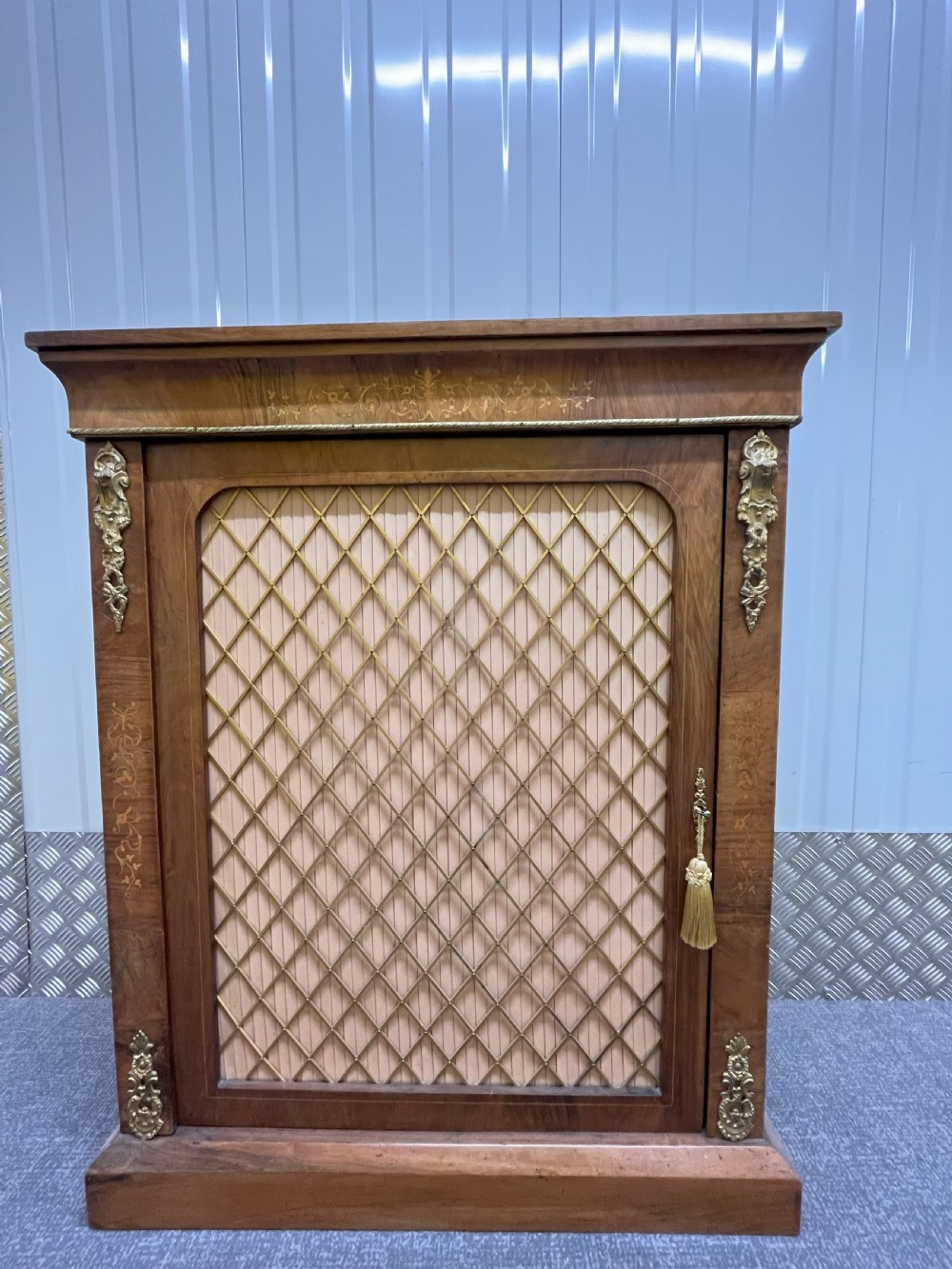A Regency rosewood side cabinet featuring a brass lattice door with pleated fabric backing, ornate brass mounts, and brass marquetry inlays. View XI