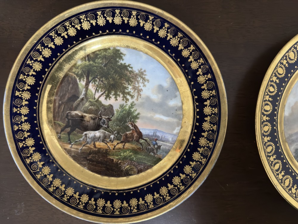 A pair of circular French Empire porcelain cabinet plates featuring hand-painted pastoral scenes surrounded by heavy gilded borders on cobalt blue. View III