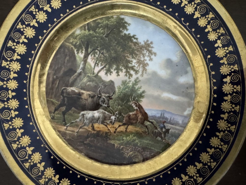 A pair of circular French Empire porcelain cabinet plates featuring hand-painted pastoral scenes surrounded by heavy gilded borders on cobalt blue. View VI
