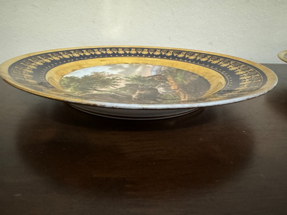 A pair of circular French Empire porcelain cabinet plates featuring hand-painted pastoral scenes surrounded by heavy gilded borders on cobalt blue. View VIII