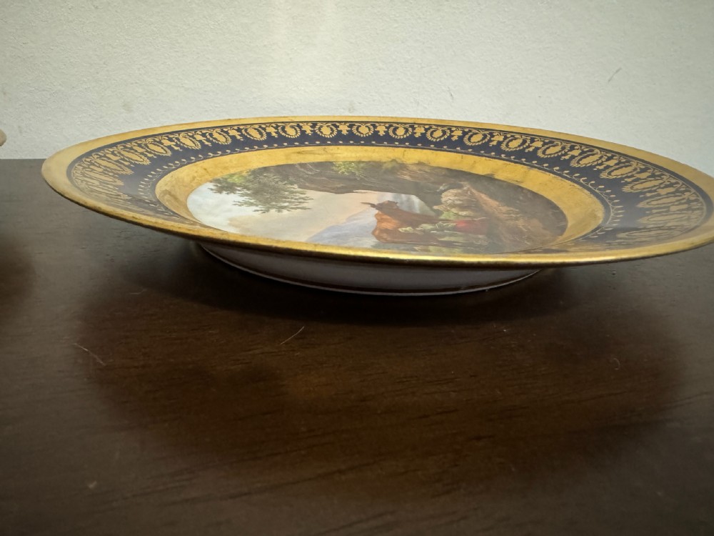 A pair of circular French Empire porcelain cabinet plates featuring hand-painted pastoral scenes surrounded by heavy gilded borders on cobalt blue. View IX