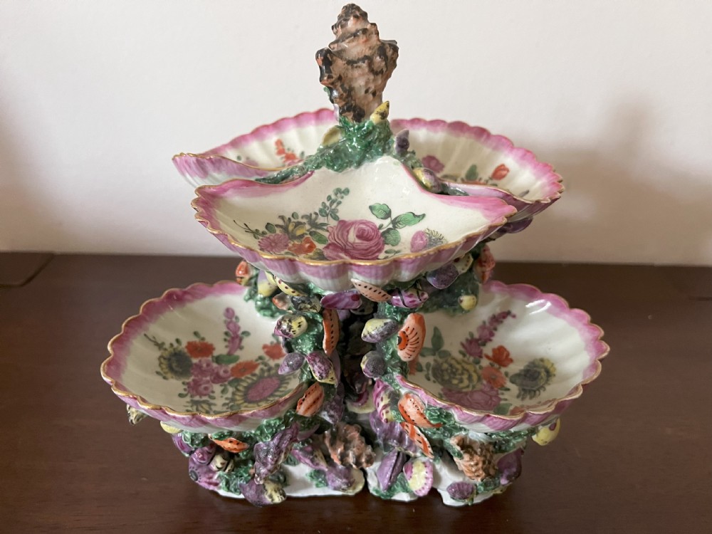 A multi-tiered 18th-century porcelain sweetmeat stand composed of shell-shaped dishes supported by a column encrusted with miniature shells and painted with floral motifs.