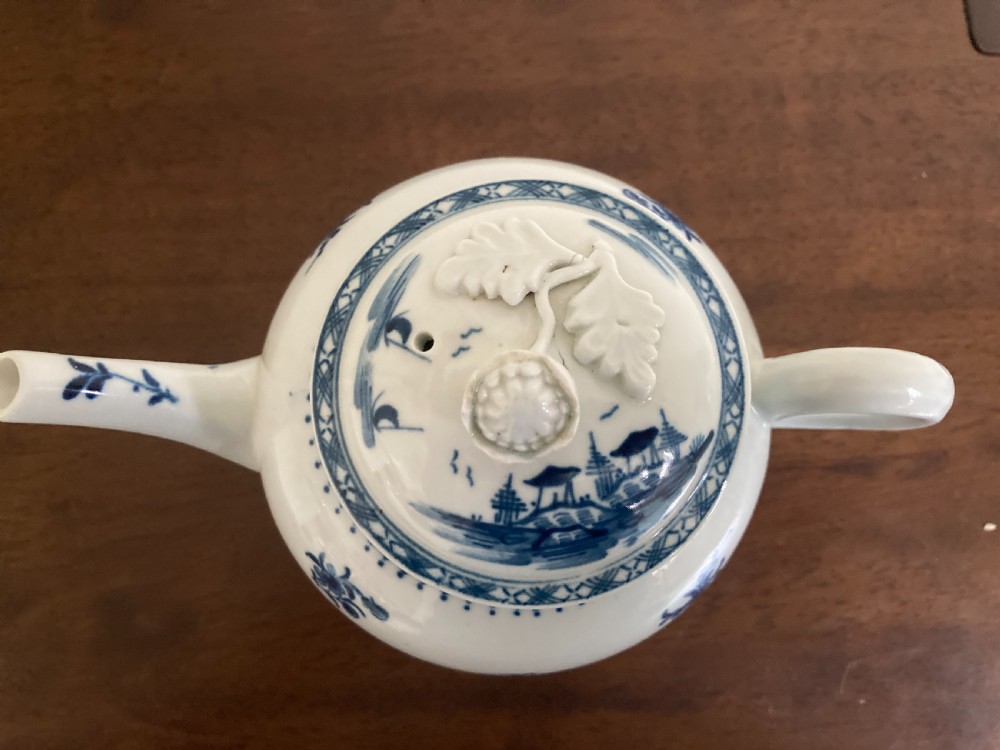 An 18th-century First Period Worcester blue and white soft-paste porcelain teapot featuring a painted chinoiserie figure, domed lid, and floral knop. View X