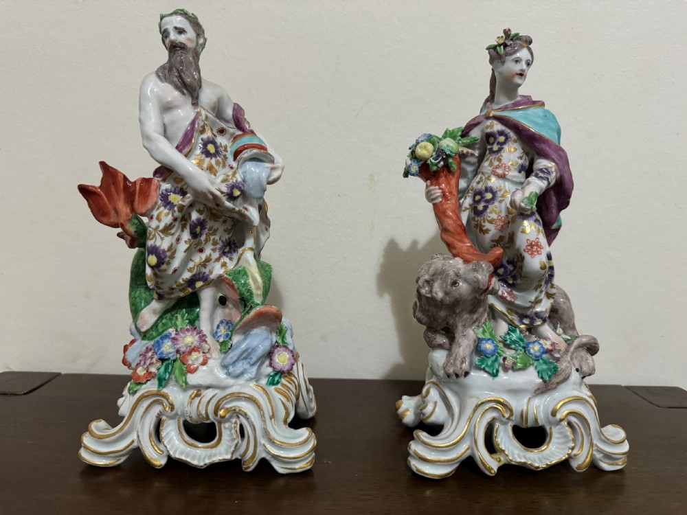 A pair of 18th-century polychrome porcelain allegorical figures depicting Water and Land resting on gilded Rococo scroll bases.