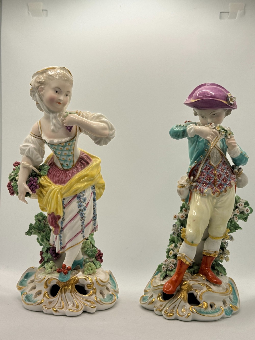 A pair of painted hard-paste porcelain figures depicting allegorical representations of Autumn and Spring standing on pierced Rococo bases.