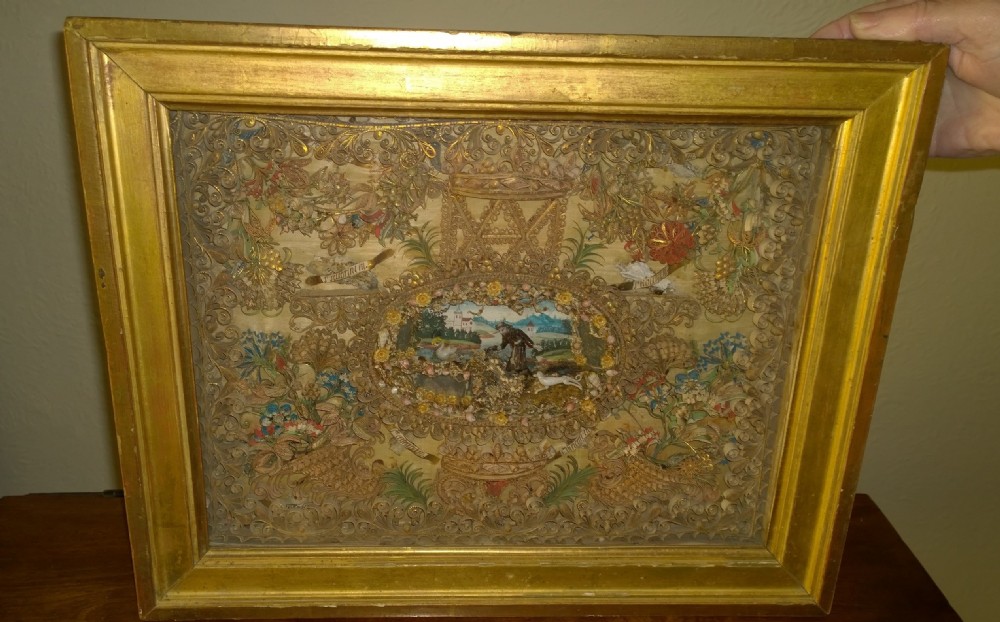 An 18th-century French giltwood framed shadow box containing intricate paperoles scrollwork surrounding a central miniature landscape with Nevers glass figures.