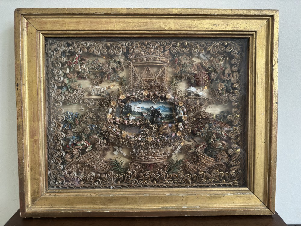 An 18th-century French giltwood framed shadow box containing intricate paperoles scrollwork surrounding a central miniature landscape with Nevers glass figures. View II