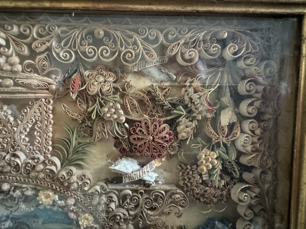An 18th-century French giltwood framed shadow box containing intricate paperoles scrollwork surrounding a central miniature landscape with Nevers glass figures. View V