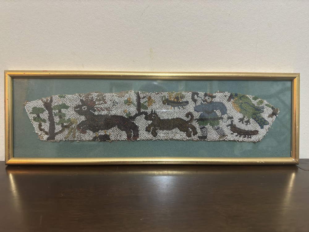 A horizontal framed 17th-century glass beadwork fragment depicting a hunting figure and animals, mounted against a green backdrop within a slim gilt frame.