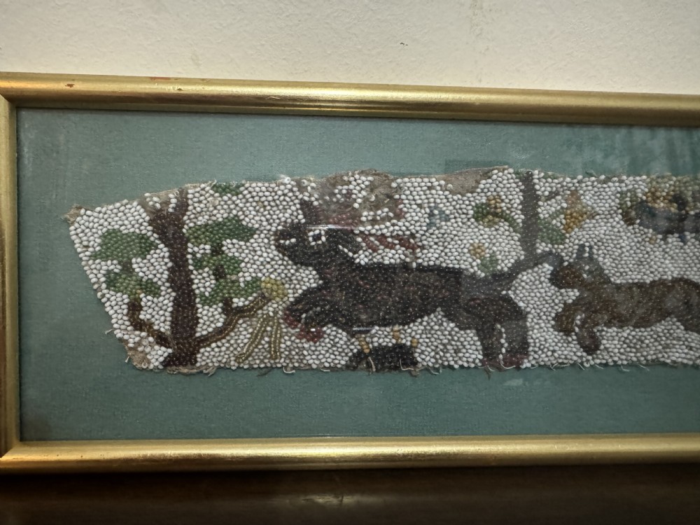 A horizontal framed 17th-century glass beadwork fragment depicting a hunting figure and animals, mounted against a green backdrop within a slim gilt frame. View II