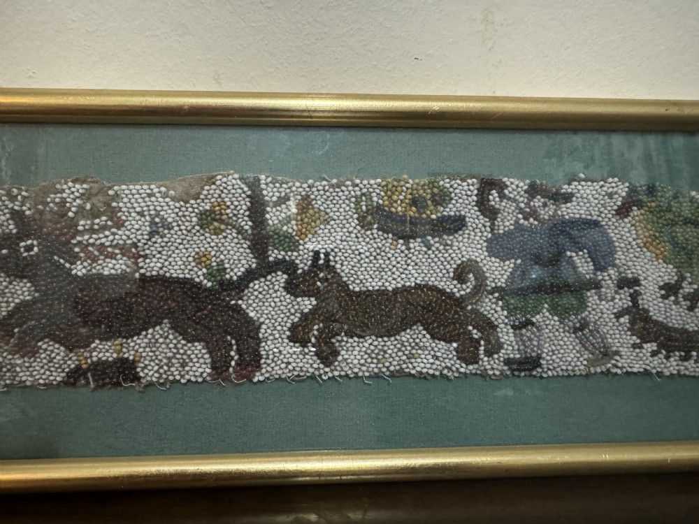 A horizontal framed 17th-century glass beadwork fragment depicting a hunting figure and animals, mounted against a green backdrop within a slim gilt frame. View III