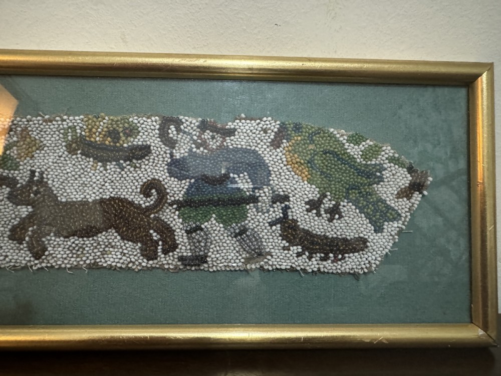 A horizontal framed 17th-century glass beadwork fragment depicting a hunting figure and animals, mounted against a green backdrop within a slim gilt frame. View IV