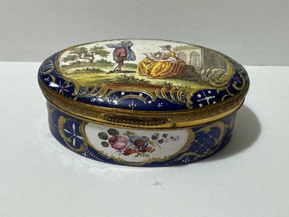 An open eighteenth-century oval Bilston enamel patch box with a cobalt blue ground, hand-painted floral cartouche, gilded borders, and white interior. View II