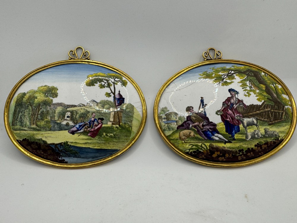 Pair of 18th-century oval South Staffordshire enamel plaques featuring hand-painted pastoral scenes set within gilt metal mounts.