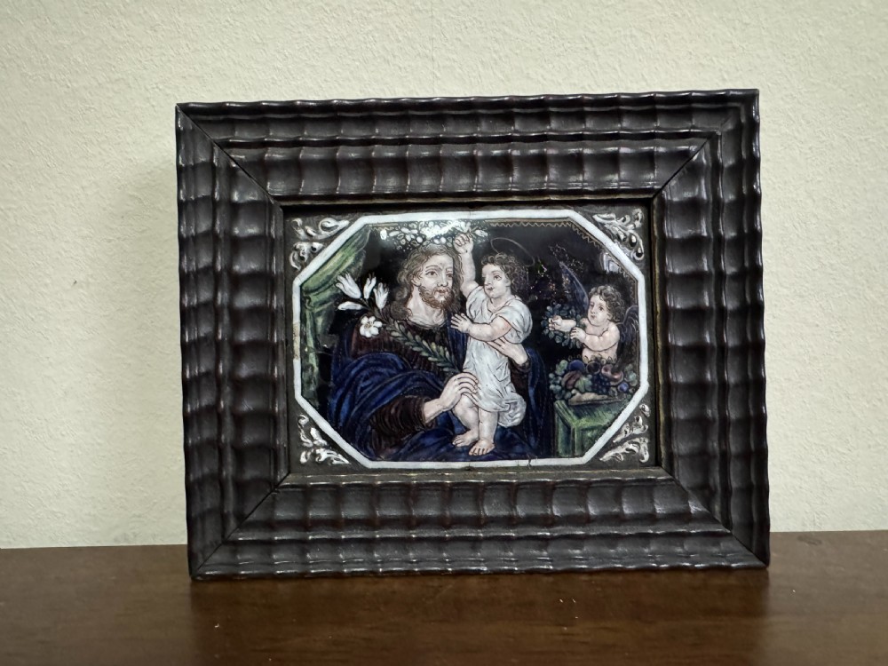 An early eighteenth-century painted Limoges enamel plaque depicting Saint Joseph and the Christ Child, set within a dark ripple-moulded wooden frame.