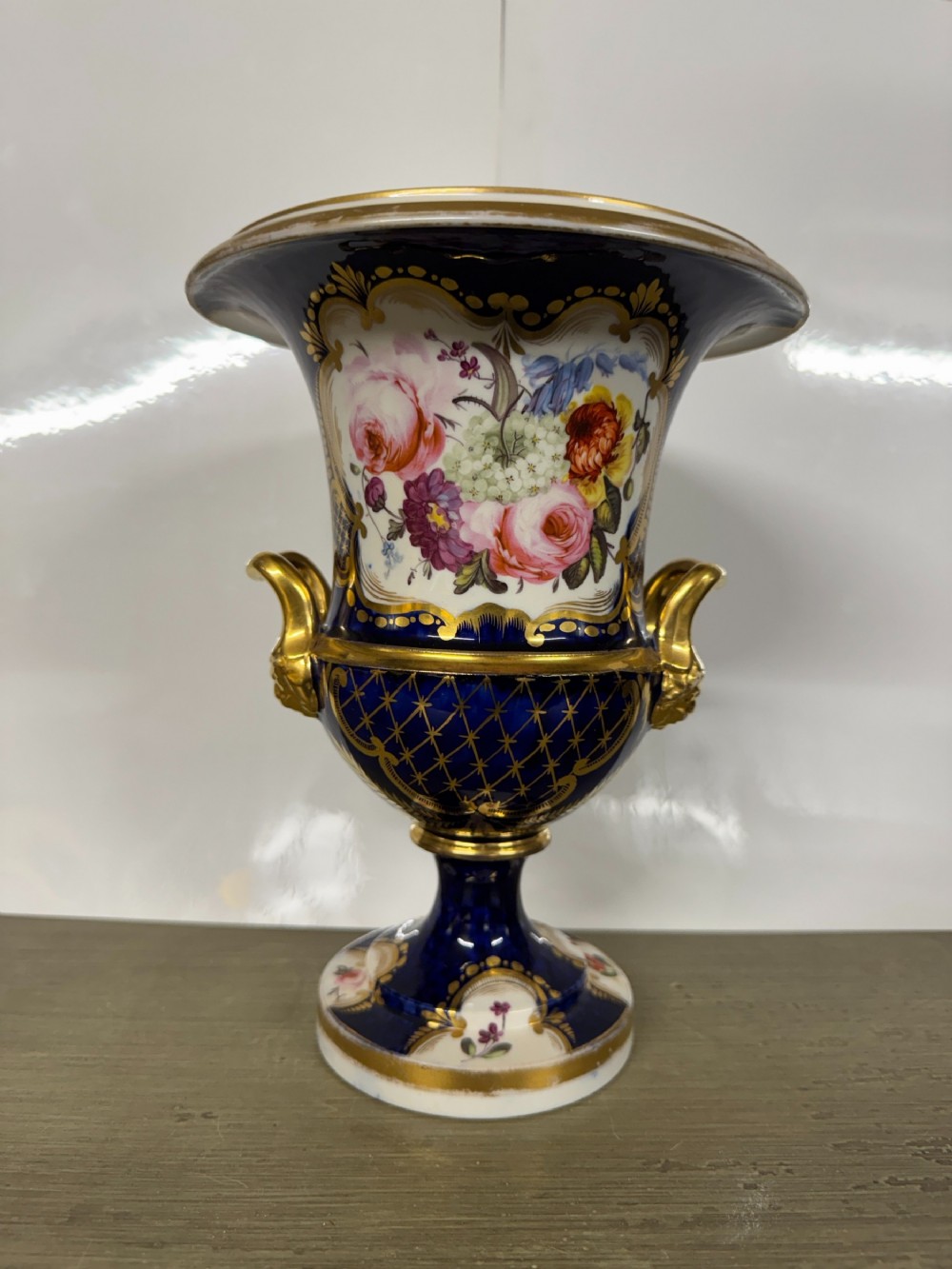 A nineteenth-century Coalport porcelain campagna urn featuring a cobalt blue ground, hand-painted floral reserve, and heavy gilding.