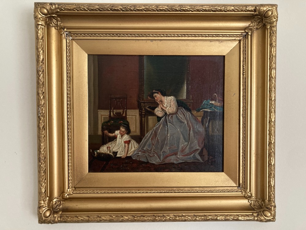 A nineteenth-century oil painting on canvas in an ornate gold frame depicting a mother watching a child play with a cat inside a period domestic interior.
