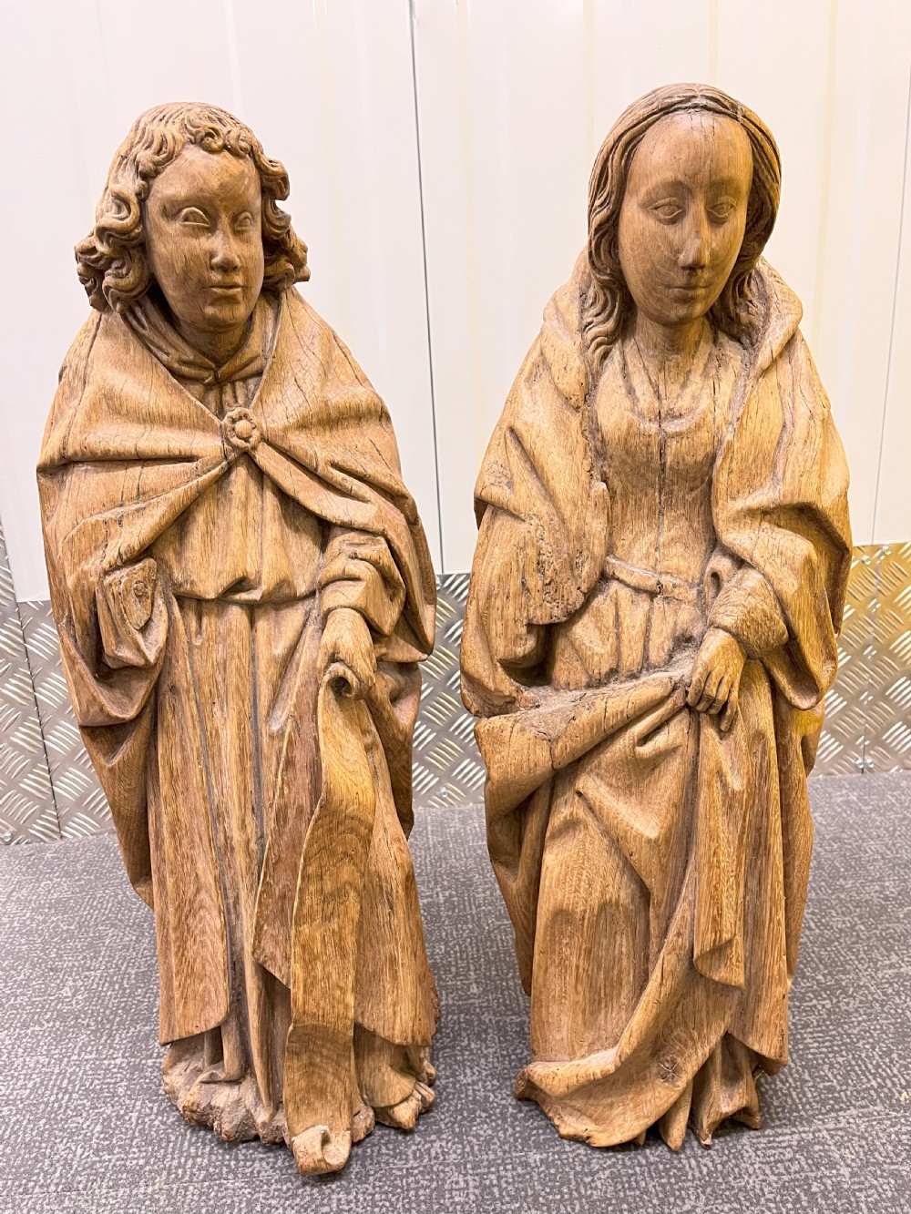 A pair of hand-carved oak sculptures depicting two standing saints in long draped robes.