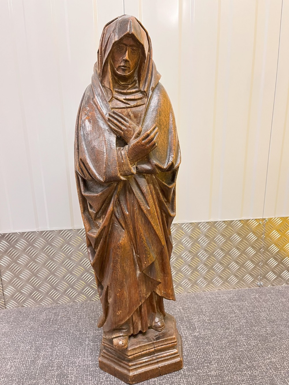 Carved dark oak sculpture depicting a hooded woman in draped robes with hands crossed over her chest, standing on an octagonal wooden base.