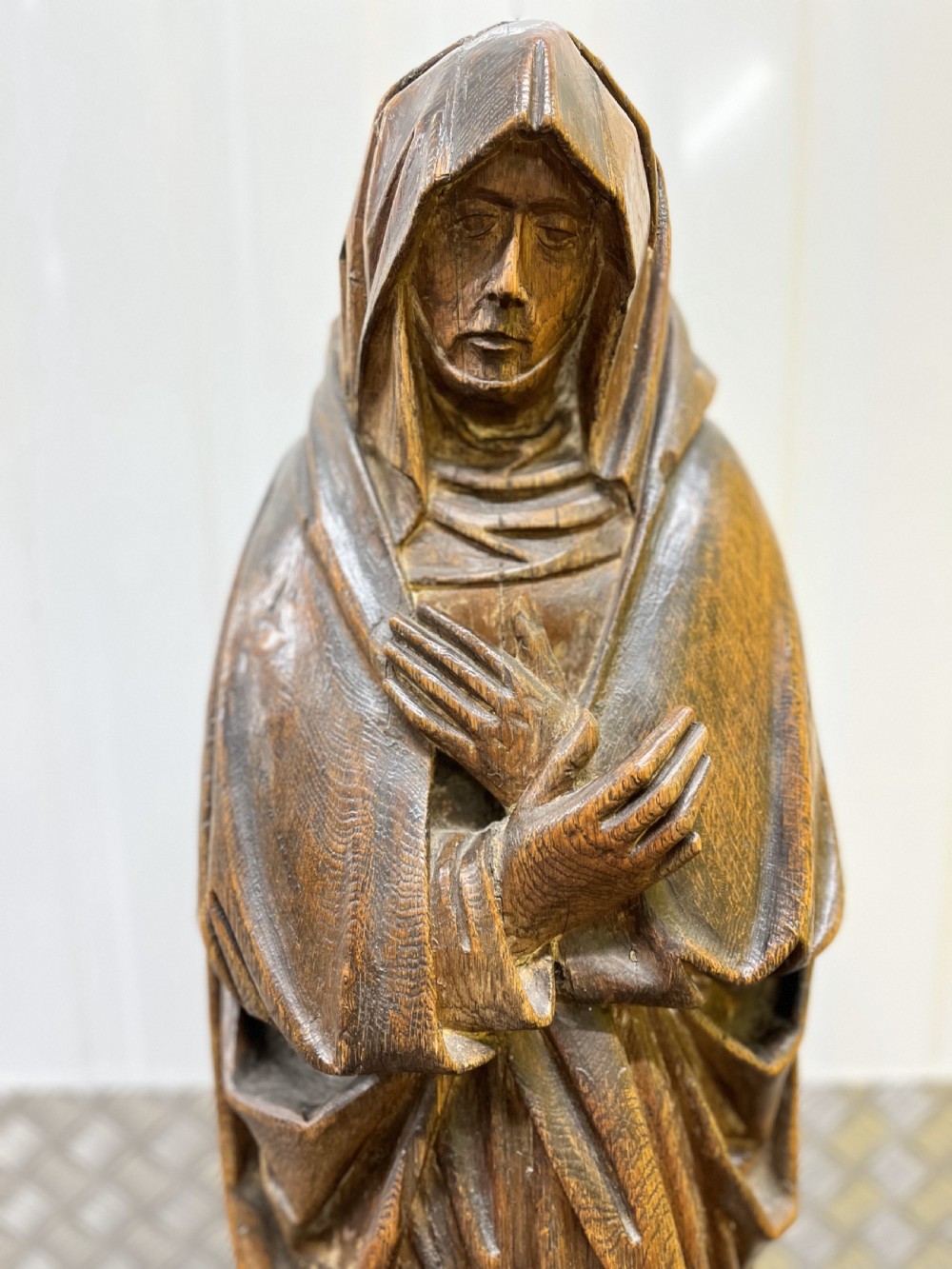Carved dark oak sculpture depicting a hooded woman in draped robes with hands crossed over her chest, standing on an octagonal wooden base. View II