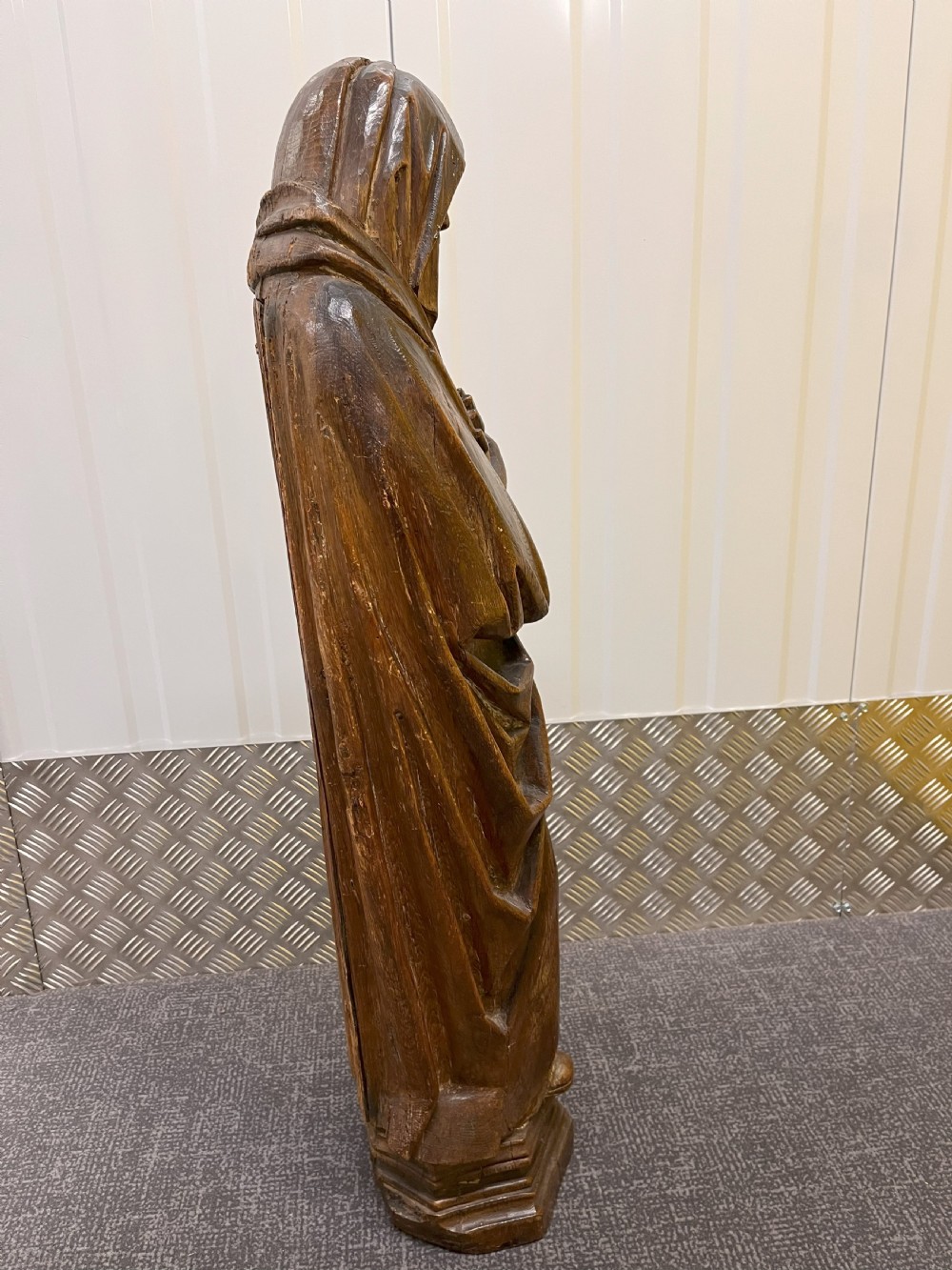 Carved dark oak sculpture depicting a hooded woman in draped robes with hands crossed over her chest, standing on an octagonal wooden base. View III