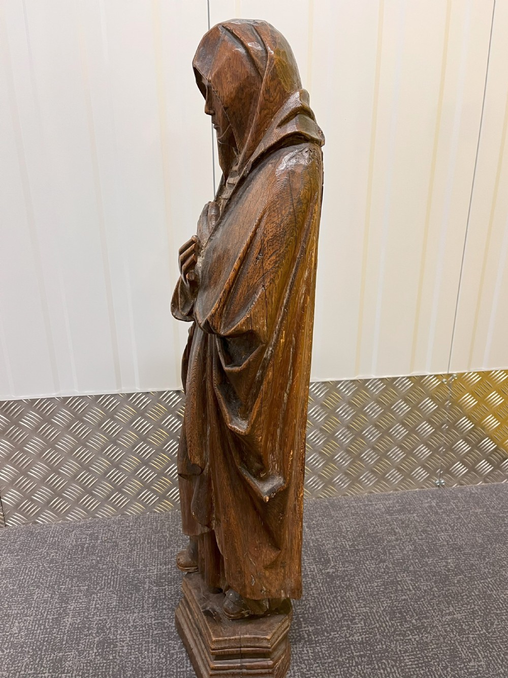 Carved dark oak sculpture depicting a hooded woman in draped robes with hands crossed over her chest, standing on an octagonal wooden base. View V