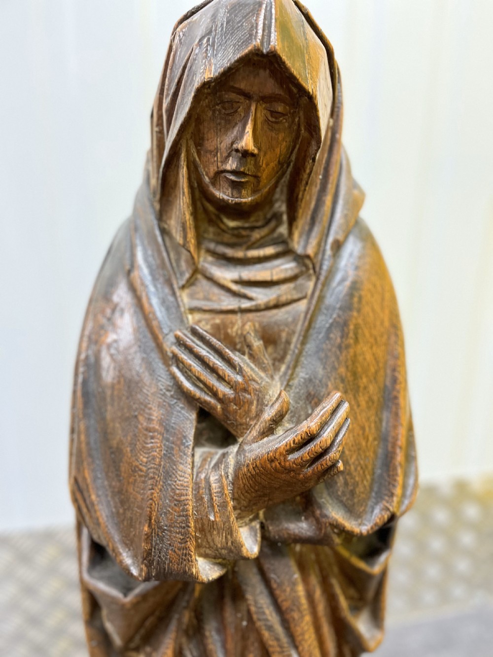 Carved dark oak sculpture depicting a hooded woman in draped robes with hands crossed over her chest, standing on an octagonal wooden base. View VI