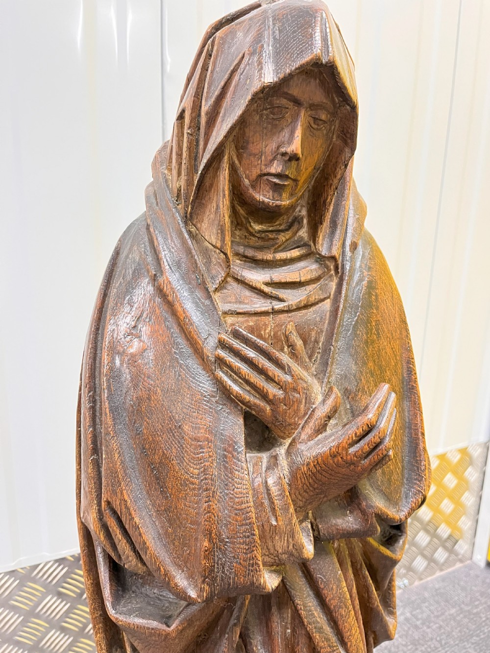 Carved dark oak sculpture depicting a hooded woman in draped robes with hands crossed over her chest, standing on an octagonal wooden base. View VII