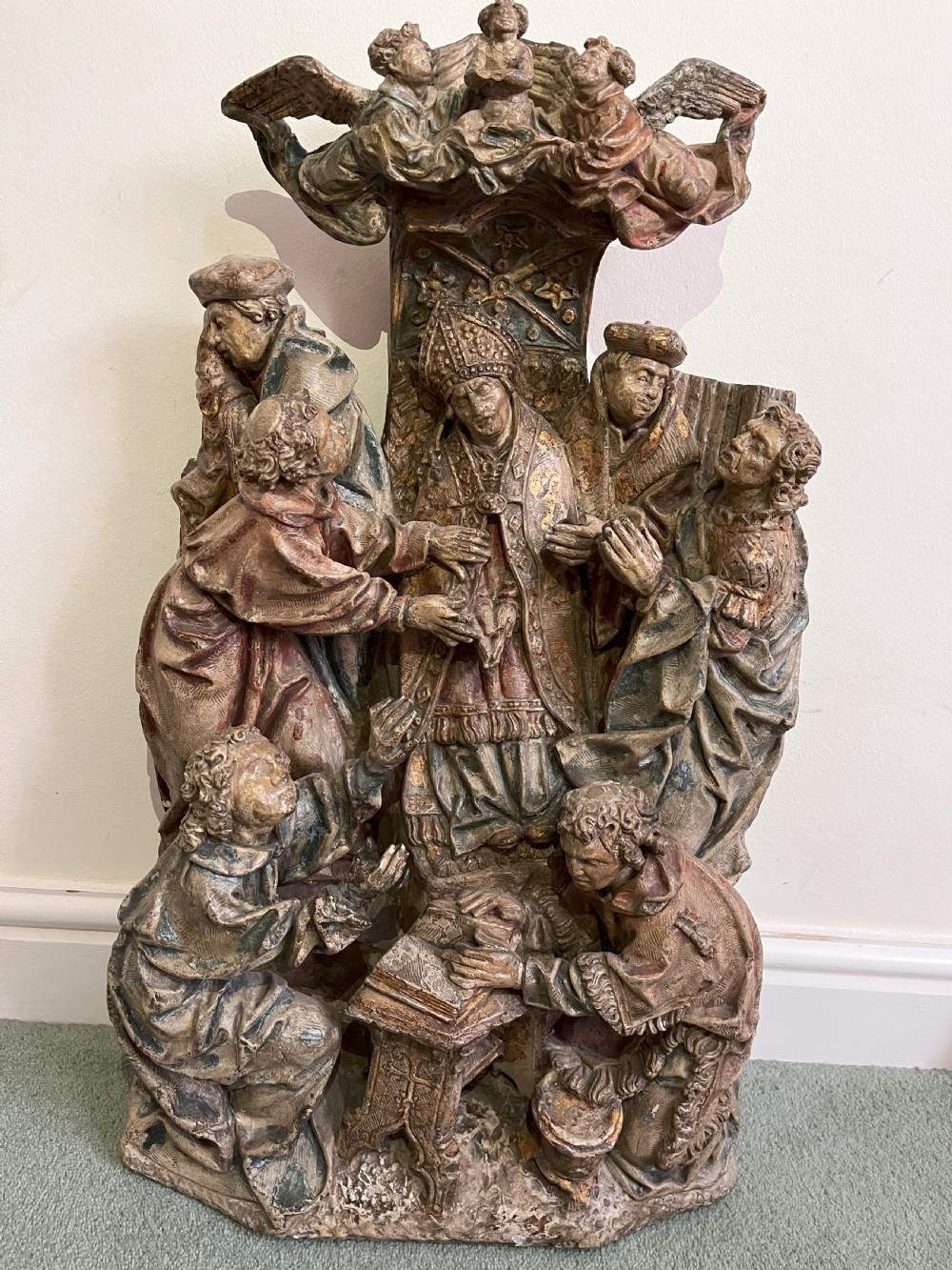 An early 16th-century carved stone relief depicting multiple figures gathered around a seated prelate with sculpted angels above.