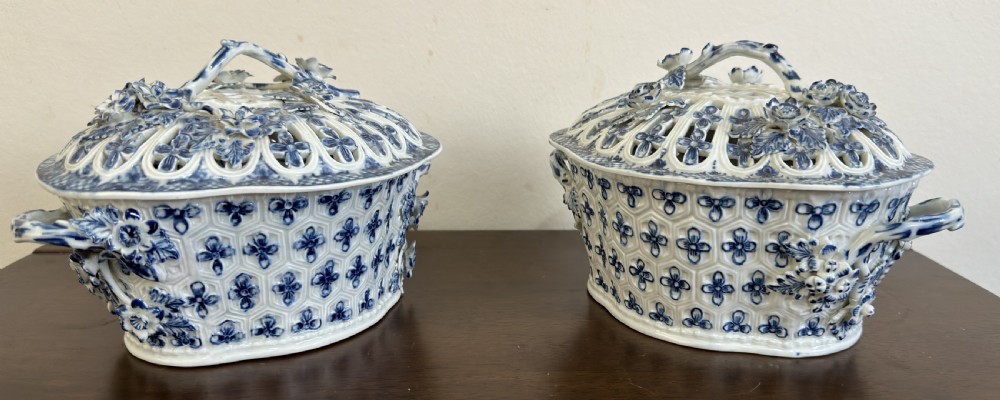 A pair of 18th-century Worcester blue and white porcelain chestnut baskets with reticulated covers, twig handles, and encrusted floral decorations.